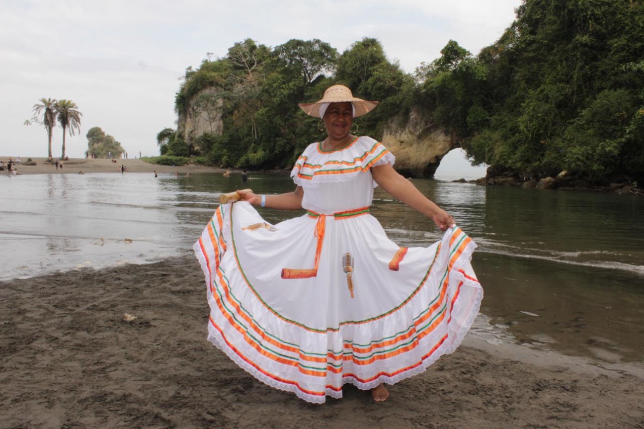 Cantaora de Sonidos Profundos con vestido tradicional blanco levantando su sombrero junto al manglar