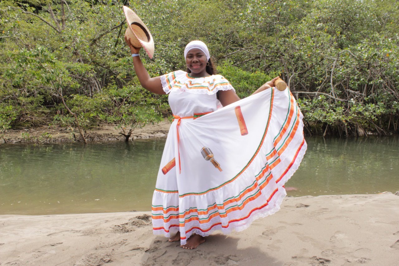 Cantaora de Sonidos Profundos con vestido tradicional blanco, sombrero y maracas, en la playa